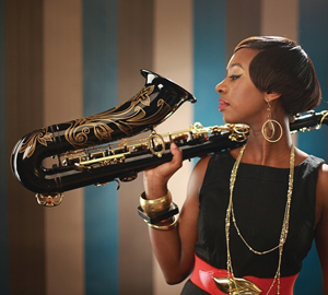 A black lady in a dress holding a saxophone over her shoulder